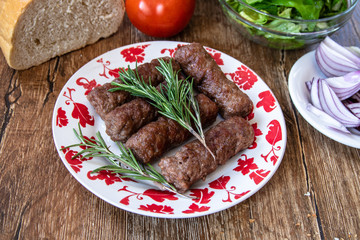 Barbeque Kebab, traditional middle eastern and mediterranean eat from minced meat on the grill with lettuce, tomato and red onion on wooden table.