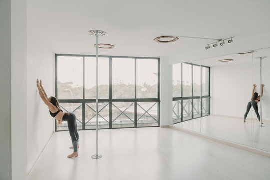 Young slim sportive woman stretching near big windows in light room studio
