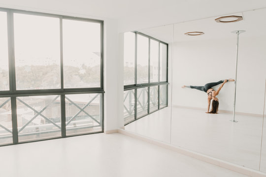 Back view of young sportive woman doing handstand and leg split in light room