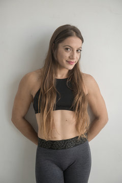 Attractive athletic woman in sportswear looking at camera standing near white wall