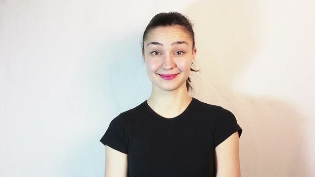 A beautiful young girl in a black t-shirt smiles and flirts raises her eyebrows while looking into the camera. Portrait on white background.
