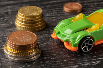 Car toy and euro coins on a dark wooden background.
