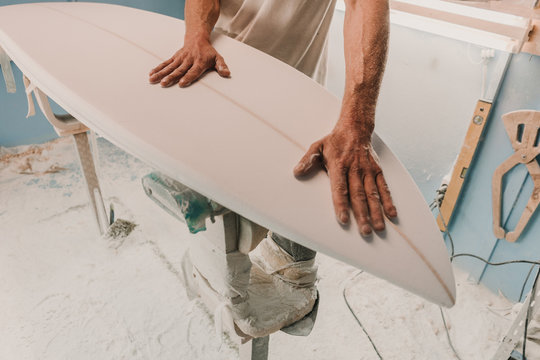 Crop male holding wooden surf board placed on stand in workplace