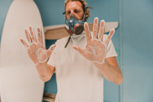 Male in breather showing palms in wooden dust near surf board in workplace