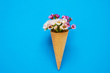 Ice cream cone with small flowers on blue background. Copy space, top view.