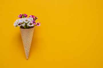 Ice cream cone with small flowers on yellow background. Copy space, top view.