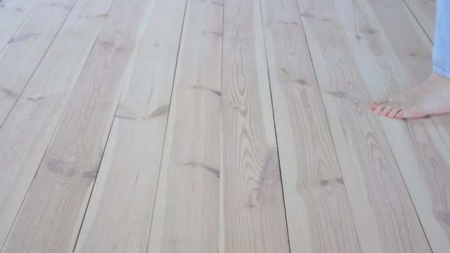 eco-friendly flooring - woman with bare feet strokes the warm wooden floor closeup.