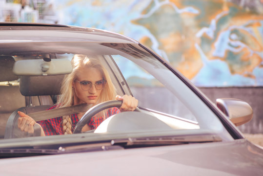 Attractive blonde girl driving a car is nervous, pulls the seat belt, tired of city traffic jams.