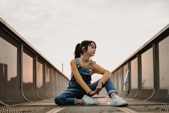Girl sitting on skateboard on walkway