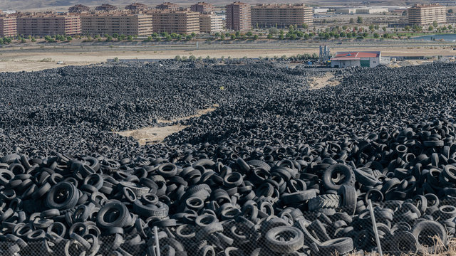 Huge pile of old auto tires between meadow near town and cloudy sky in sunny day