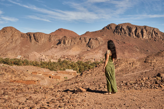 Back view of young brunette lady standing between desert lands near ancient constructions and hills in Marrakesh, Morocco