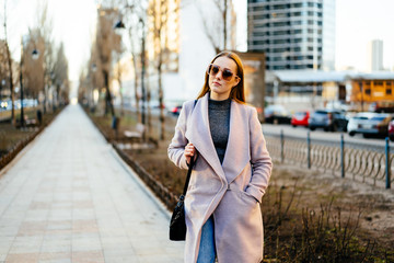 Beautiful young caucasian woman walking along the street in the city. Stylish female model wearing sunglasses walking on city street.