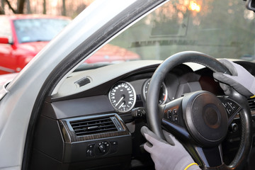 Dłonie kierowcy w rękawiczkach na kierownicy samochodu osobowego.