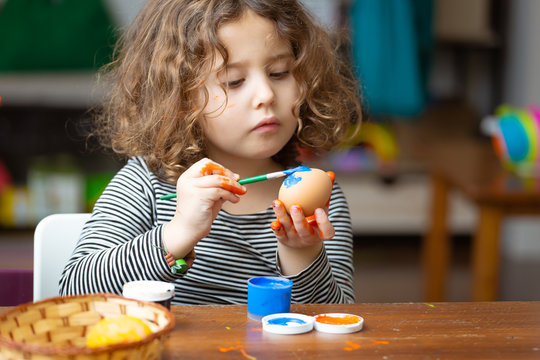 Toddler girl painting egg at table