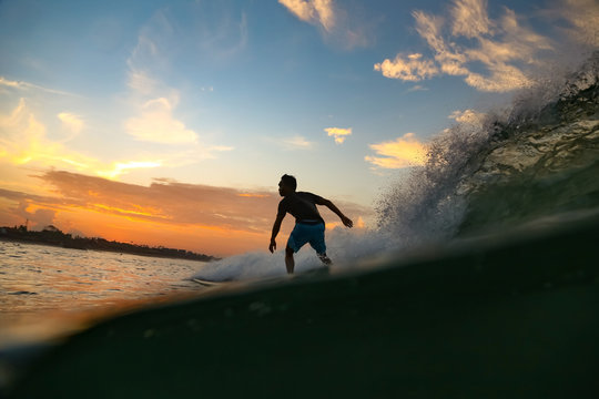 Male surfing between waving water of sea with splashes and cloudy sky in evening on Bali, Indonesia