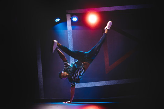 Modern ethnic man in denim and white sneakers showing contemporary dance in handstand position