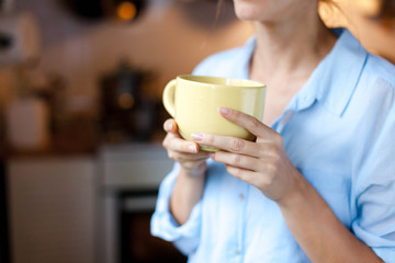 Graceful female hands hold mug of tea. Young woman is drinking coffee in cozy home kitchen. Close up.