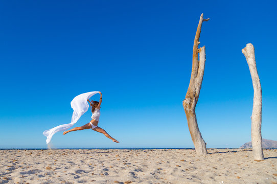 Side view of attractive woman jumping with pareo on sandy beach inn sunny cloudless day