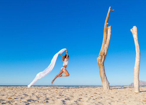 Side view of attractive woman jumping with pareo on sandy beach inn sunny cloudless day