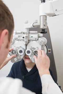 Optician testing a boy's eyes with optometry devices
