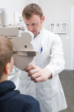 Optician testing a boy's eyes with optometry devices