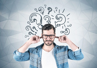 Young man covering ears, question marks