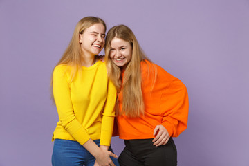 Two pretty happy young blonde twins sisters girls in vivid colorful clothes standing looking camera isolated on pastel violet blue wall background. People family lifestyle concept. Mock up copy space.