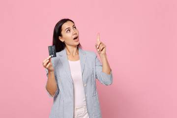 Thinkful young woman looking up pointing index finger up with great new idea holding credit bank card isolated on pink pastel background. People sincere emotions lifestyle concept. Mock up copy space.