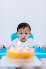 Cute little boy with birthday cake sitting on chair in room . mother holding birthday cake with candle in front of baby sitting in high chair .