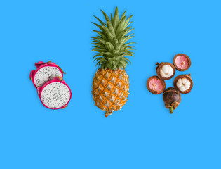 Fresh exotic fruits, arranged on the blue background. Pink dragon fruit, yellow pineapple and purple mangosteen. Healthy dietary food. Vitamins and antioxidants.