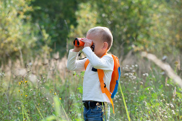Young explorer watching with binoculars of birds in the high grass