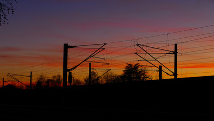 Fototapeta na wymiar Bahngleise, Oberleitungen, Silhouette mit Bäumen, im Sonnenuntergang 