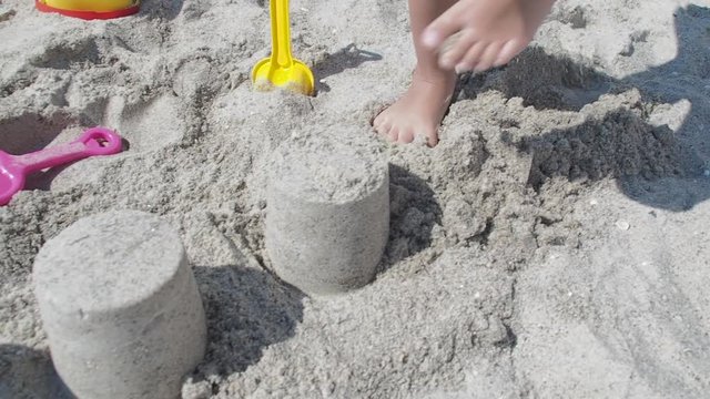 Child breaking sandcastles. The child's feet are crushing the sand structure.