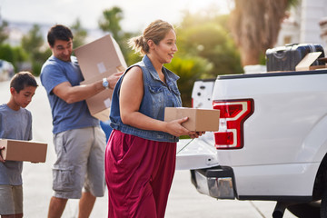 hispanic family moving boxes out of pickup truck into house - obrazy, fototapety, plakaty