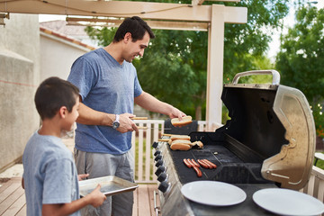 father and son grilling hot dogs together on backyard gas grill