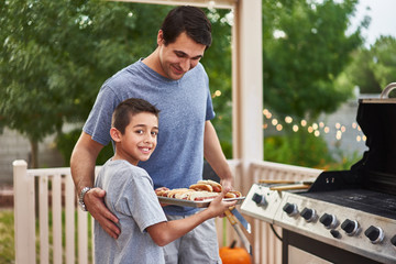 proud father and son showing tray of grilled hot dogs