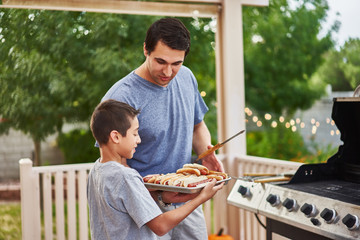 father and son grilling hot dogs together on backyard gas grill - Powered by Adobe