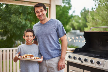 proud father and son showing tray of grilled hot dogs