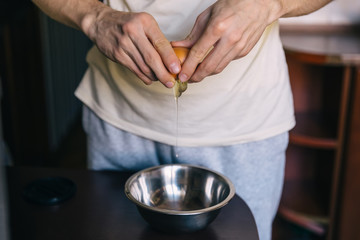 chef cooking in the kitchen. broken egg in hands. bowl on the ta