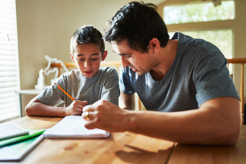 father helping son with homework on table at home - obrazy, fototapety, plakaty