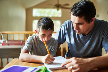father helping son with homework on table at home
