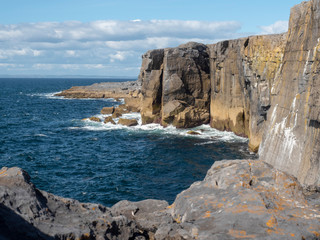 Fototapeta na wymiar Mini cliff, county Clare, Ireland, Sunny day. Atlantic ocean. Tourist bus and tourists explore the area.
