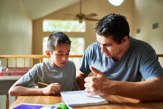 father helping son with homework on table at home