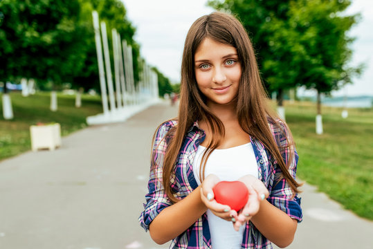 Happy student student girl holding a toy heart summer city. Free space text. Background of road green trees. Concept of love, blood and organ donation, give life. Save man Smile joy and tenderness.