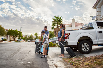 hispanic family loading luggage into back of pickup truck in front of house for travel