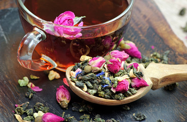 a cup of tea. green tea with flowers in a wooden spoon on a dark wooden table. green tea with flowers and dry fruit pieces. blend tea. close up