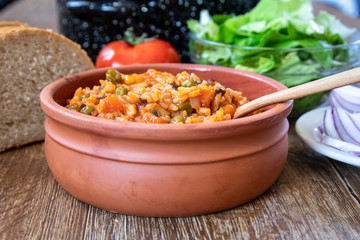 Fried rice with vegetables and spices in a vintage clay bowl and tomato, lettuce, onion and bread on wooden table