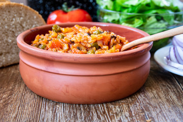 Fototapeta na wymiar Fried rice with vegetables and spices in a vintage clay bowl and tomato, lettuce, onion and bread on wooden table