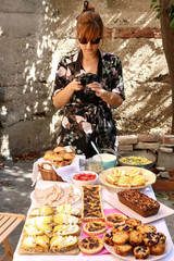 Food blogger photographing brunch food - croissants, scrambled eggs, ham, banana bread, blueberry muffins, sandwiches and mushroom tart. Outdoor, natural light, selective focus. 