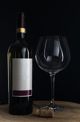 Red wine glasses and bottle on a wooden plate with black background.